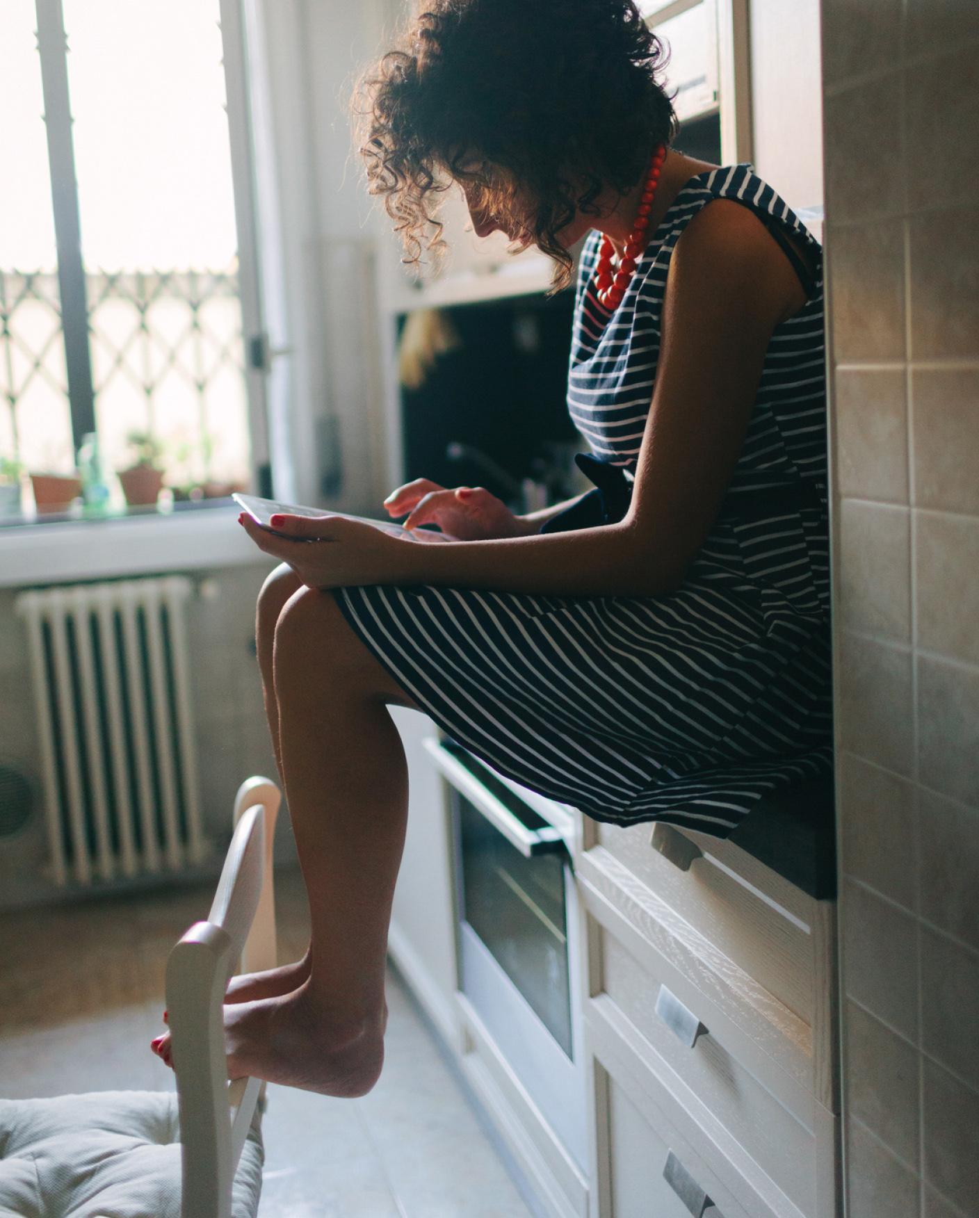 girl sits on counter with ipad in lap and feet on chair